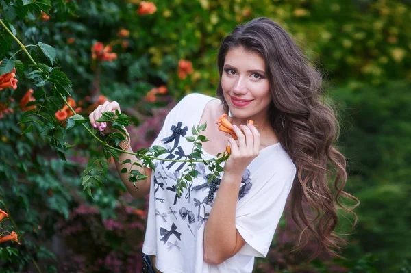 Красива молода жінка з довгим кучерявим волоссям позує біля квітів в саду — стокове фото
