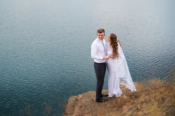 Unga vackra paret bruden och brudgummen på bröllop promenad vid sjön — Stockfoto