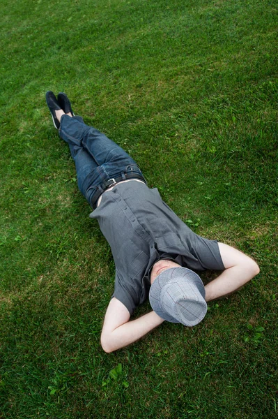 Homme d'affaires couché dans un champ sur de l'herbe verte avec le chapeau sur le visage. Revenus passifs — Photo