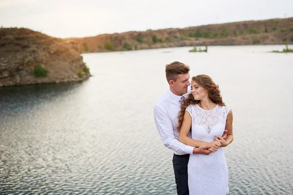 Unga vackra paret bruden och brudgummen på bröllop promenad vid sjön — Stockfoto