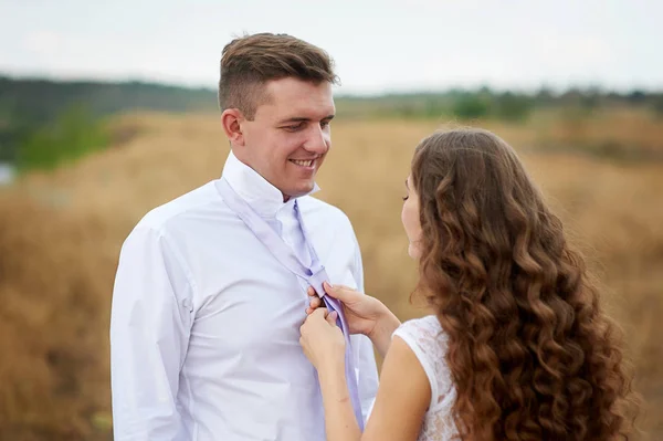 Bride dress for groom his tie on the nature in field — Stock Photo, Image