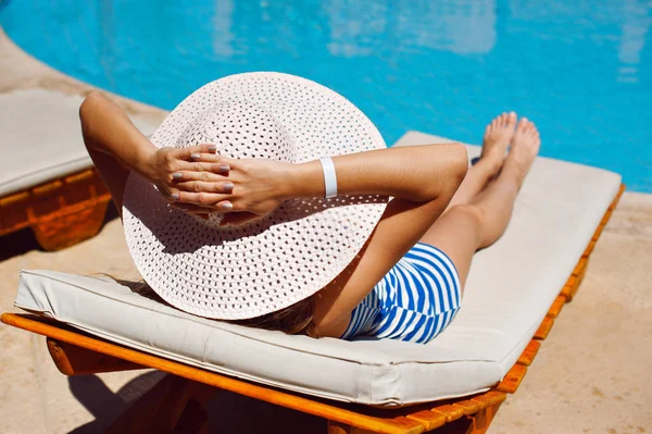 Bela mulher em um chapéu branco ensolarado à beira da piscina — Fotografia de Stock