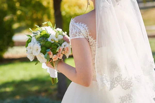 Bride with wedding bouquet of white roses on walk in park stands back — Stock Photo, Image