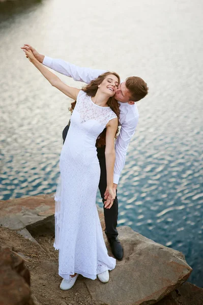 Braut und Bräutigam umarmen sich im Hintergrund des Wassers — Stockfoto