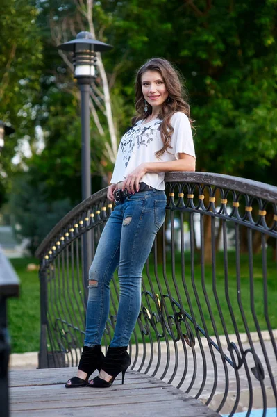 Jonge vrouw staande op de brug in spijkerbroek en een wit t-shirt — Stockfoto