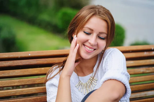 Jovem feliz sentada em um banco no parque — Fotografia de Stock