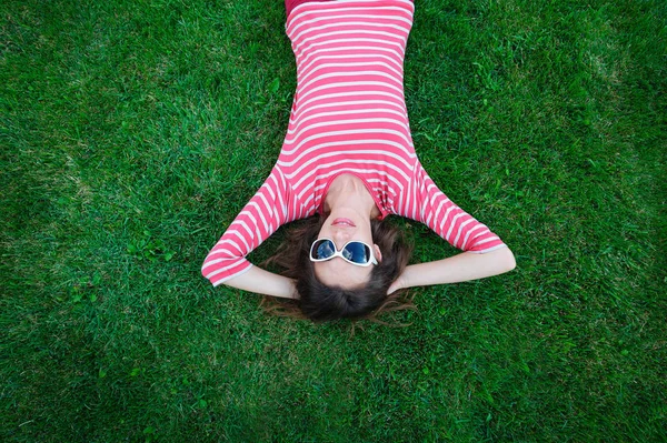 Schöne junge Frau auf dem grünen Gras auf der Wiese liegend — Stockfoto