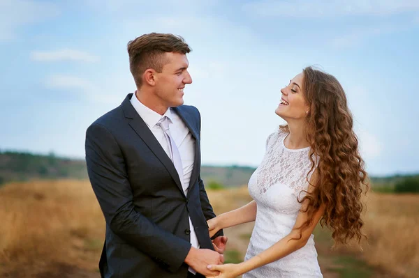 Lyckliga bruden och brudgummen promenader i ett fält i bröllopsdag — Stockfoto