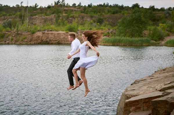 Bride and groom jumping together into the water — Stock Photo, Image