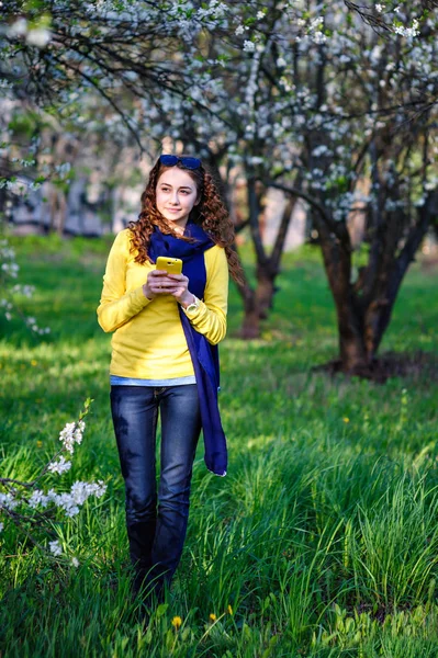 Schöne junge Frau, die mit ihrem Handy im Park spaziert — Stockfoto