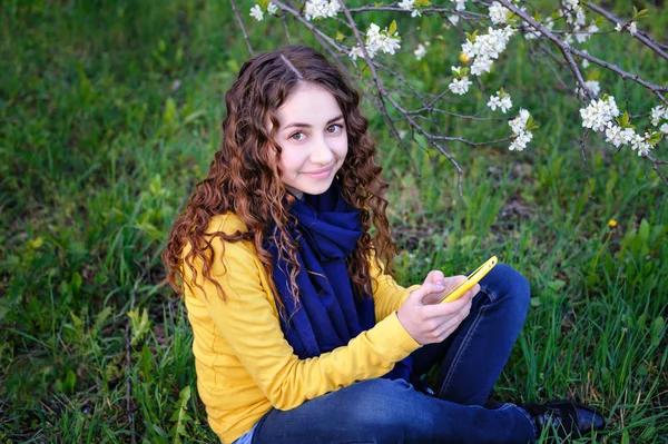 Schöne junge Frau sitzt mit Handy im Gras — Stockfoto