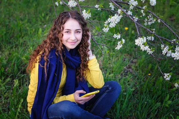 Vacker ung kvinna som sitter på gräset med telefon — Stockfoto