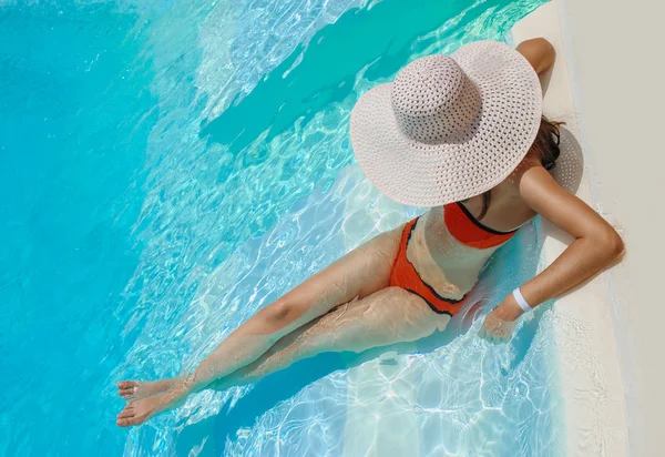 Bela mulher de chapéu branco descansa perto da piscina — Fotografia de Stock