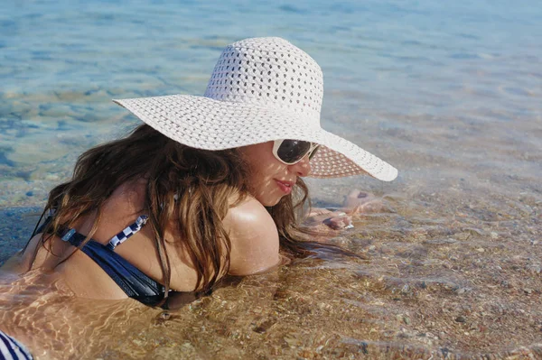 Γυναίκα σε ένα μεγάλο άσπρο καπέλο είναι στο νερό της θάλασσας — Φωτογραφία Αρχείου