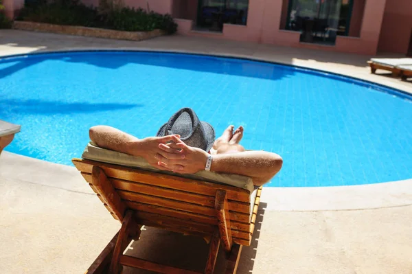 Mann mit Hut sonnt sich auf einer Liege am Pool — Stockfoto