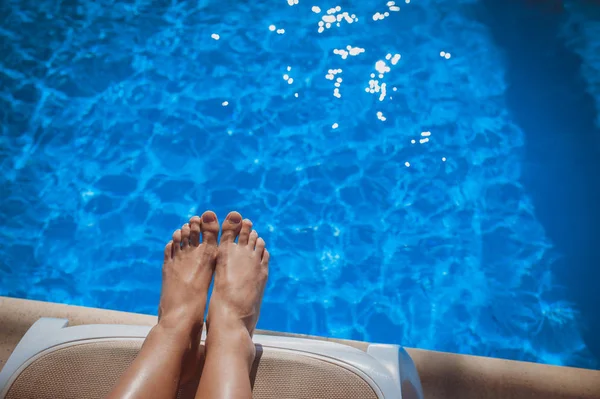 Gambe donna prendere il sole vicino alla piscina blu — Foto Stock