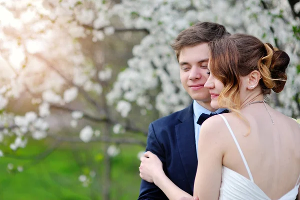 Bruid en bruidegom knuffelen in de bloemrijke lente tuin bruiloft lopen — Stockfoto