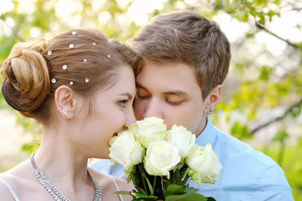 Novia y novio en el parque de primavera oliendo una rosa blanca — Foto de Stock