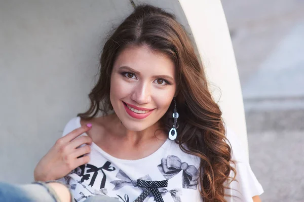 Sorrindo jovem mulher em uma camisa com maquiagem perto da parede — Fotografia de Stock