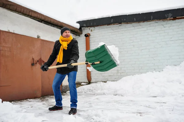 Hombre en una bufanda naranja limpia la nieve —  Fotos de Stock