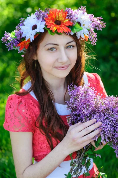 Schöne junge Frau mit einem Kranz auf dem Kopf und einem Strauß Flieder — Stockfoto