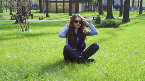 Beautiful young woman sitting on the grass in the summer park — Stock Video