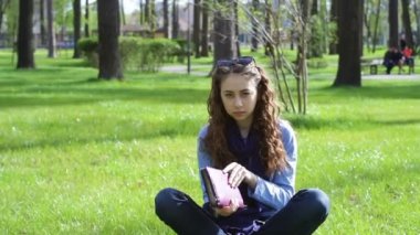 çimenlerin üzerinde bir yaz parkta güzel genç kadın kitabı kapatır ve yaprakları