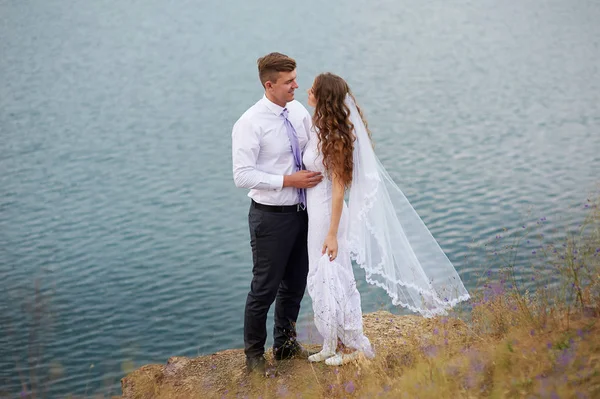 Bruden och brudgummen embracing vid sjön för en promenad — Stockfoto