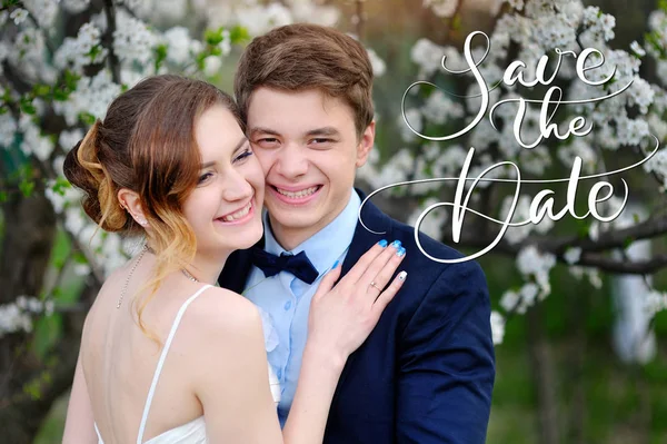 Lyckliga bruden och brudgummen i en blomstrande trädgård på våren och ord Spara datumet. Kalligrafi bokstäver — Stockfoto