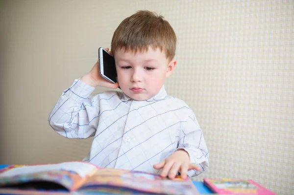 Kleine jongen zit aan Bureau en praten over de telefoon — Stockfoto