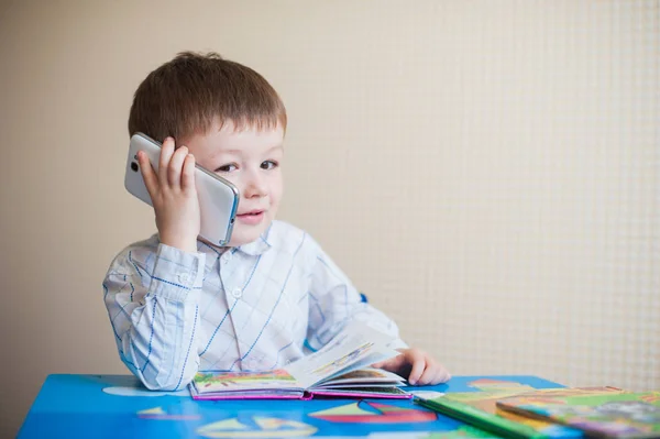 Little boy sitting at desk and talking on the phone — Stock Photo, Image