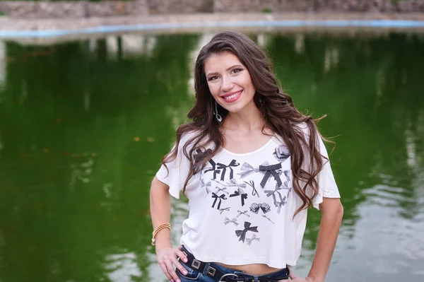 Uśmiechający się młoda kobieta, stojąc na tle jeziora w parku — Zdjęcie stockowe