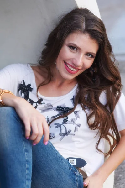 Beautiful young woman in t-shirt sitting near a gray wall — Stock Photo, Image