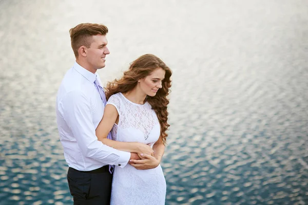 Sposa e sposo abbracciare su uno sfondo di acqua — Foto Stock