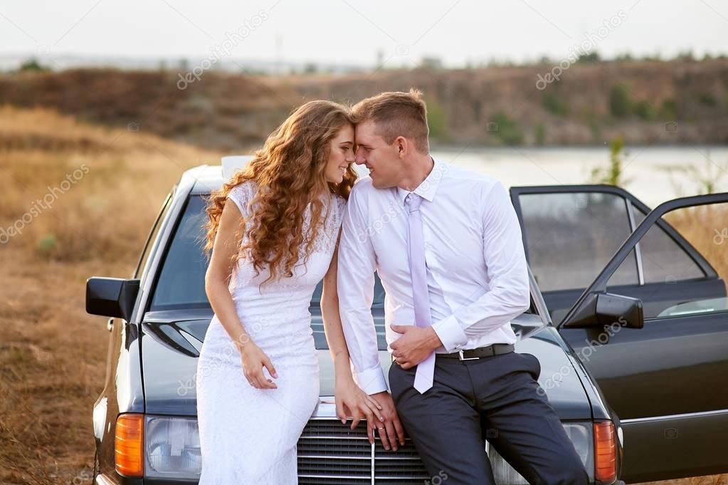bride and groom sit on the hood of the car