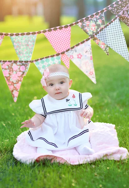 Klein meisje in witte jurk zittend op het gras in het park — Stockfoto