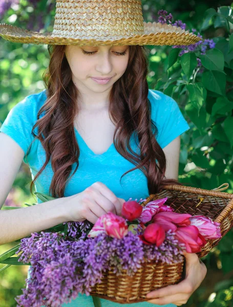 Schöne junge Frau mit Hut und einem Korb voller Flieder und Tulpen — Stockfoto