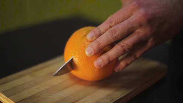Mann schneidet die Orange auf einem Holzbrett — Stockvideo