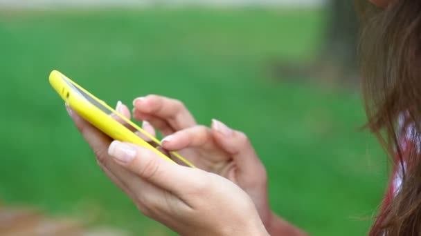 Ung kvinna sitter på en bänk i parken sommaren med en smartphone — Stockvideo