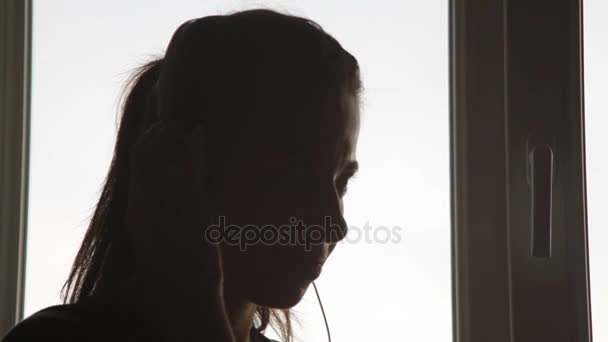 Hermosa mujer en auriculares cerca de la ventana escuchando música — Vídeo de stock