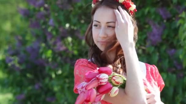 Bella giovane donna in un parco primaverile con una corona di fiori — Video Stock