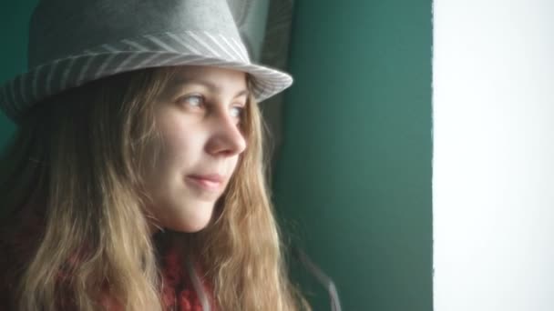 Mooie jonge vrouw in een hoed kijkt uit het raam — Stockvideo