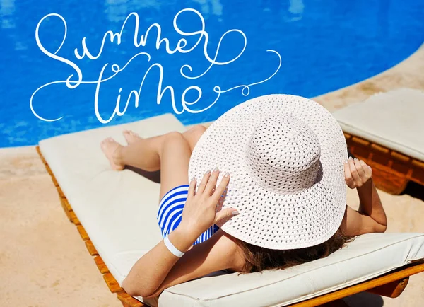 Beautiful woman in a big white hat on a lounger by the pool and text Summer time. Calligraphy lettering hand draw — Stock Photo, Image