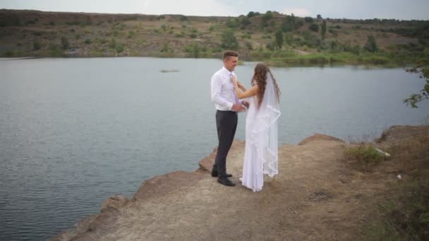 Braut und Bräutigam umarmen sich beim Hochzeitsspaziergang am See — Stockvideo