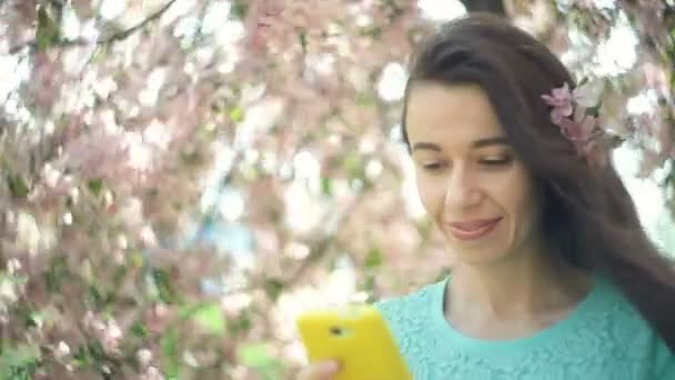 Lycklig kvinna med en telefon i en blommande våren trädgård — Stockvideo