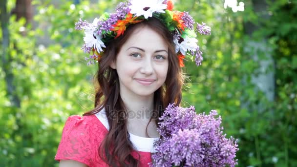 Mulher bonita com uma coroa de flores na cabeça e um buquê de lilás nas mãos — Vídeo de Stock