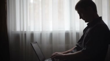 Ofiste bir pencere yakınında bir dizüstü bilgisayar ile bir adam silüeti