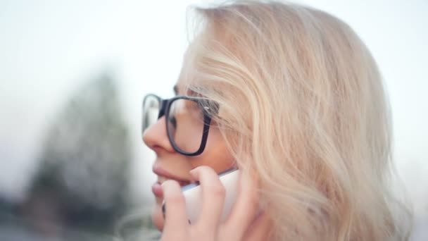 Hermosa joven con gafas está hablando por teléfono — Vídeos de Stock