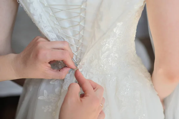 Dama de honra ajuda a vestir um vestido de noiva em uma manhã de casamento — Fotografia de Stock