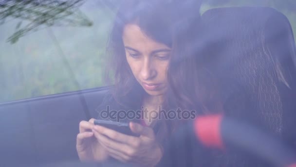 Schöne junge Frau sitzt mit Smartphone im Auto — Stockvideo